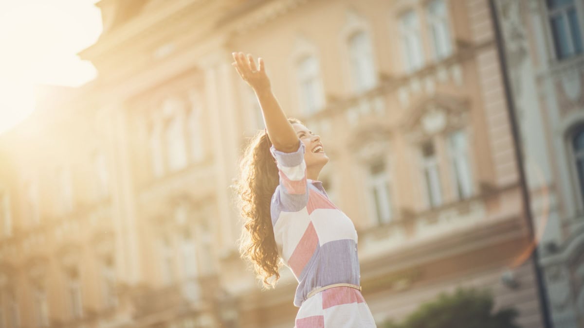 woman holding arms up in joy in front of a building