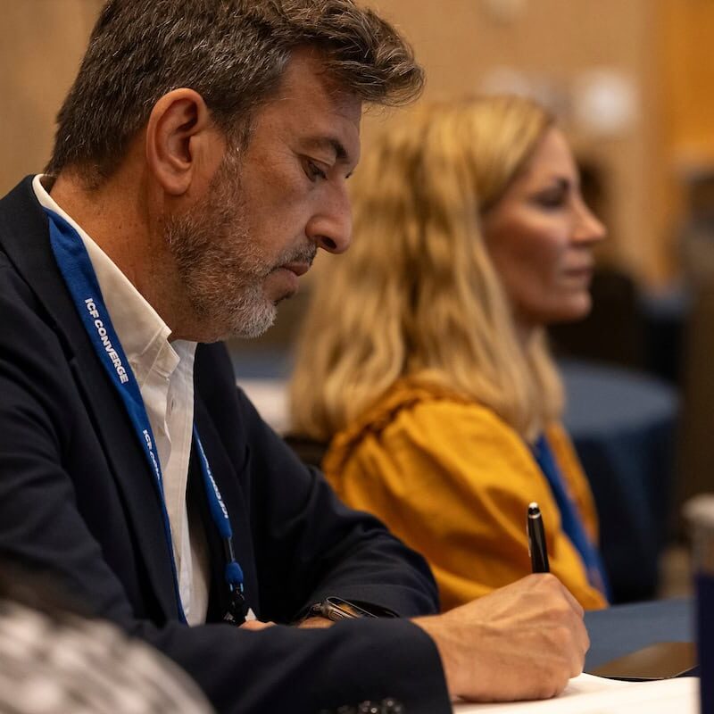 Man writing in a notebook while attending a conference session