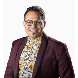Jacques Abreu PCC PHD headshot photo, dark haired man with maroon blazer yellow shirt and glasses smiling in front of white background