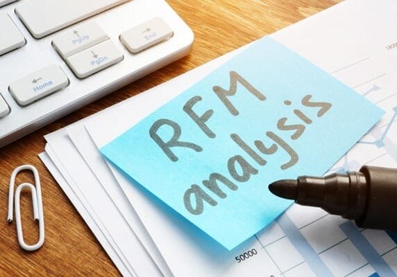 Keyboard paper clip stack of papers a marker and a sticky note stating RFM Anaysis