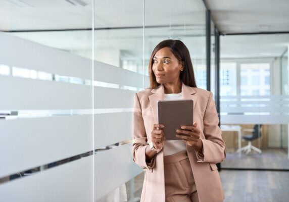 coach leaning against glass wall with tablet looking through wall and smiling