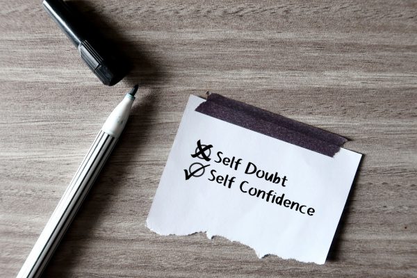 pen and marker next to piece of paper with an x next to self doubt and a check mark next to self confidence