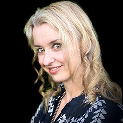 Shawna Corden PCC headshot photo, blond woman wearing dark top in front of a black background smiling