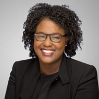 Dziko Crews headshot photo, smiling woman with dark hair and top in front of a light gray background