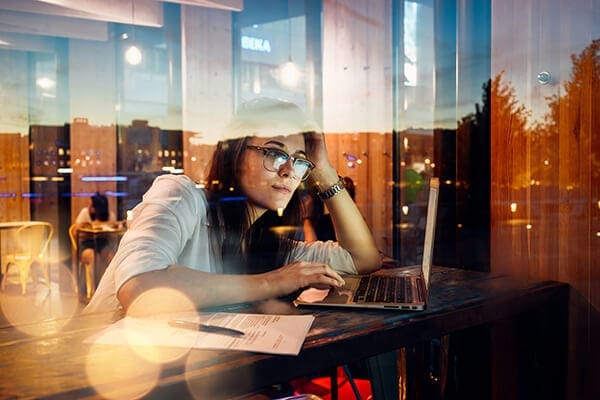 woman sitting at coffee shop window hightop working on her laptop at dusk