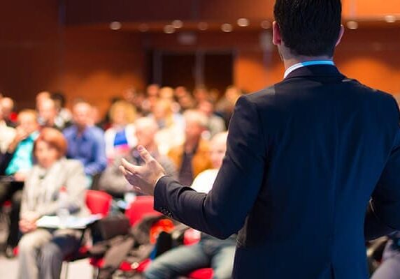 male in a suit speaking to an auditorium