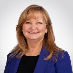 Sherrie Haynie headshot photo, woman with light brown hair purple blazer and black top smiling against a white background