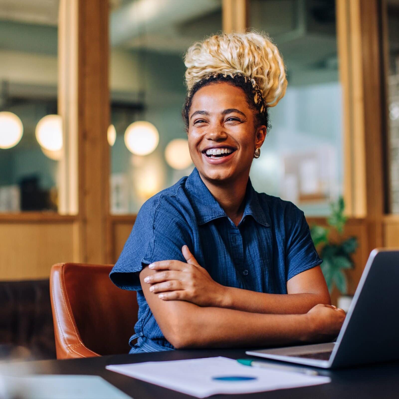 A woman working on her laptop while starring out the window thinking about her coach legacy within a professional office.
