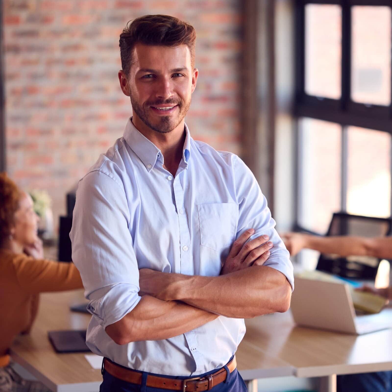 A man standing in an office, crossing his arms and staring at the user.