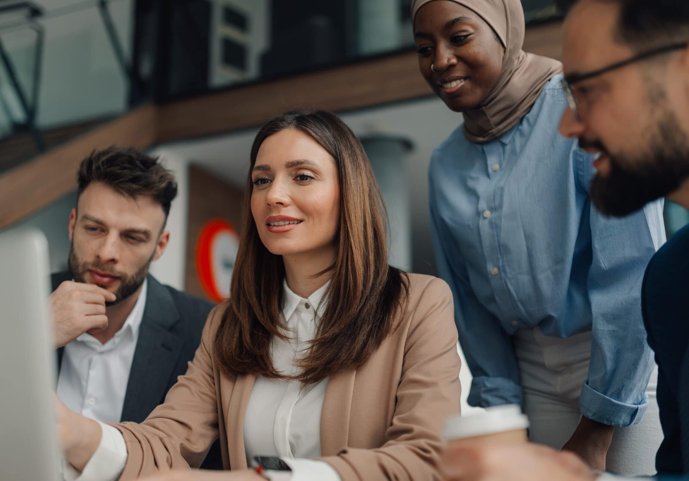 Four diverse professionals gathered around a computer collaborating on a project
