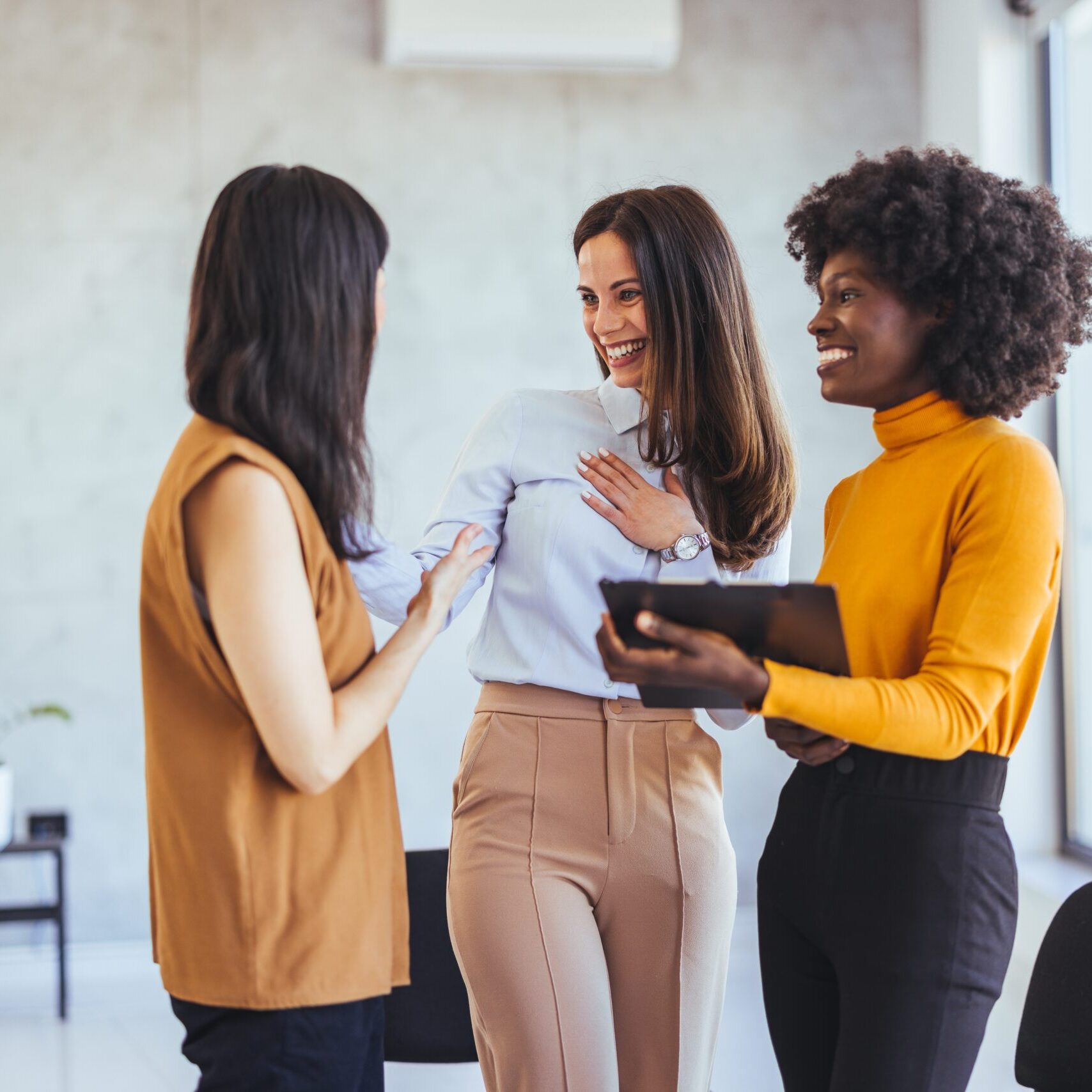Three coworkers smiling and talking while standing together in a modern office
