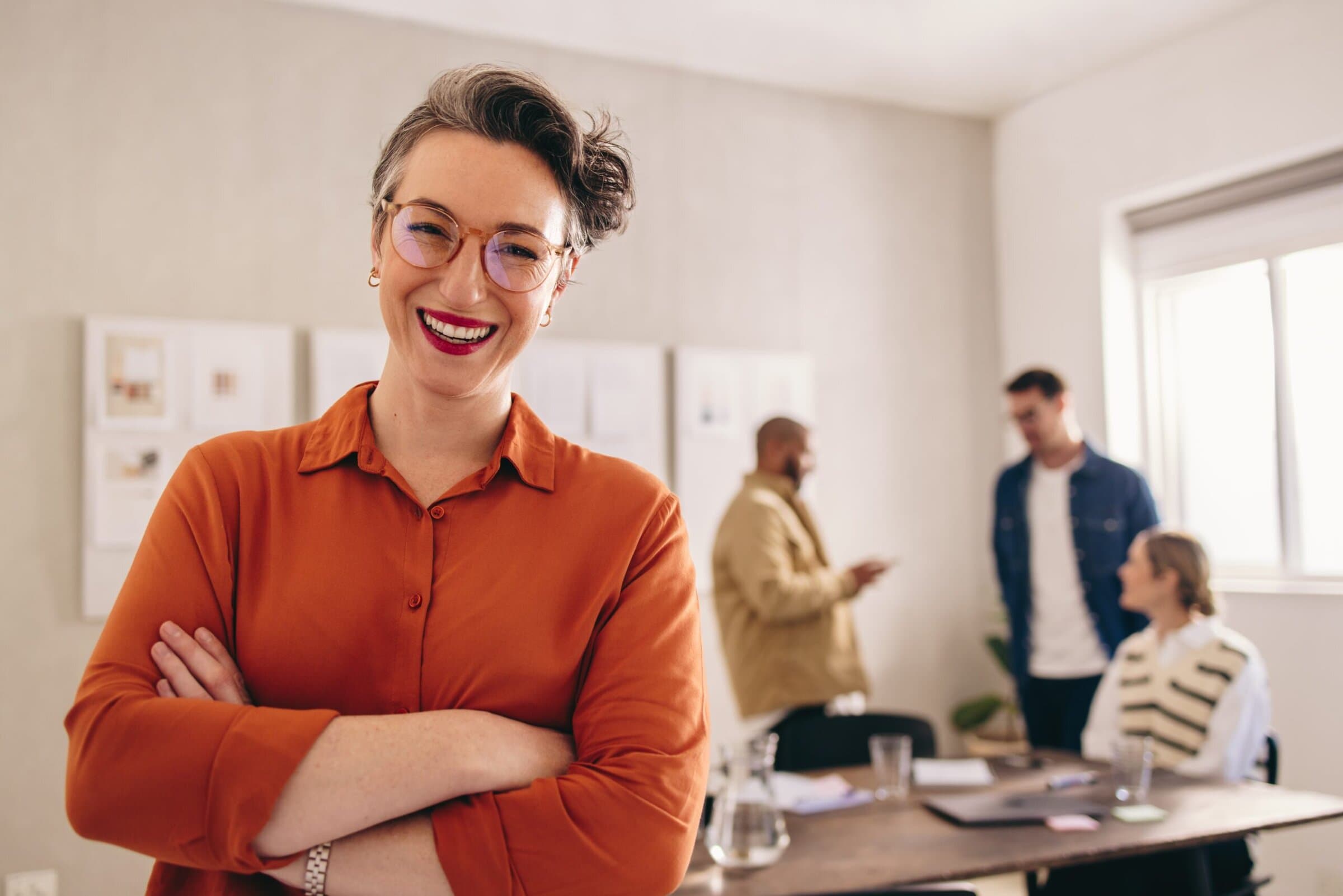 A confident professional smiles at the camera while standing in a well-lit office space.