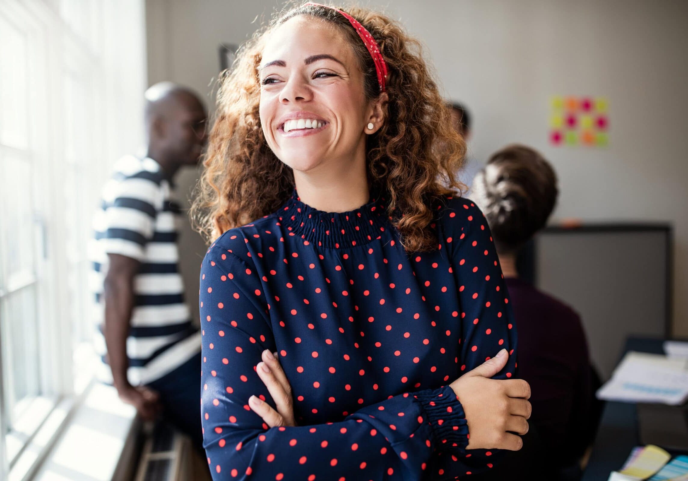 Smiling professional standing with arms crossed in a collaborative office workspace