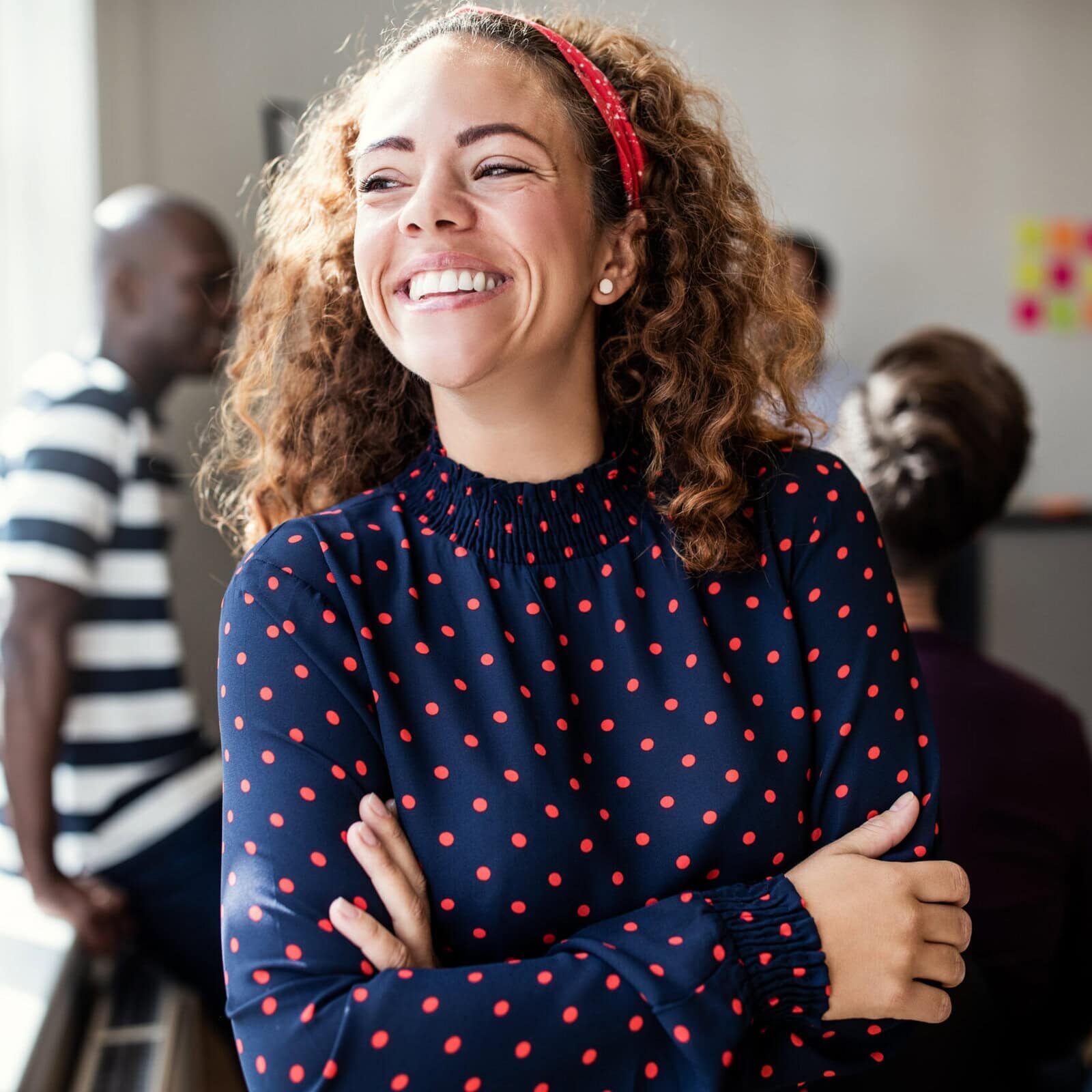 Smiling professional standing with arms crossed in a collaborative office workspace