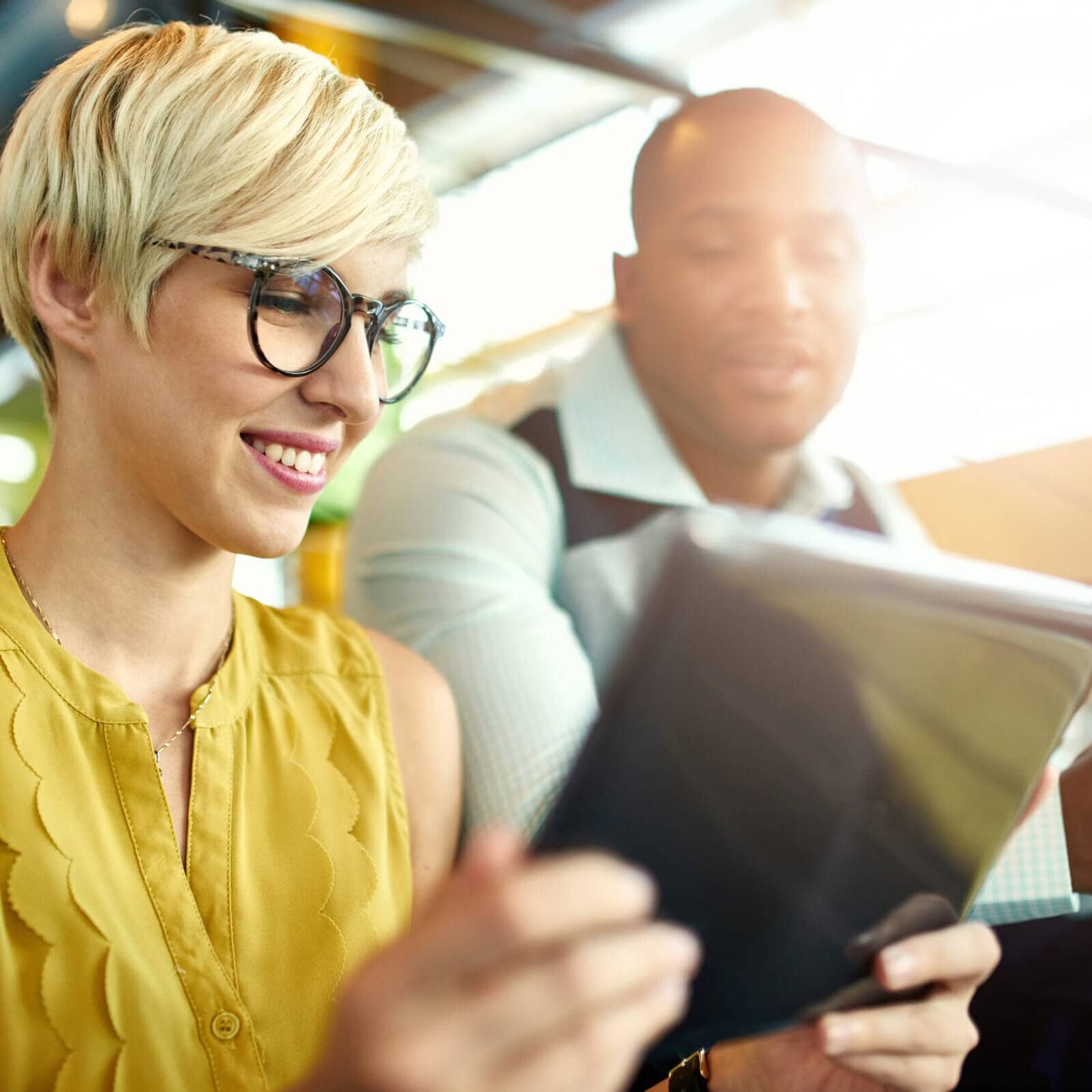 Two professionals sitting together looking at a tablet in a bright modern workspace