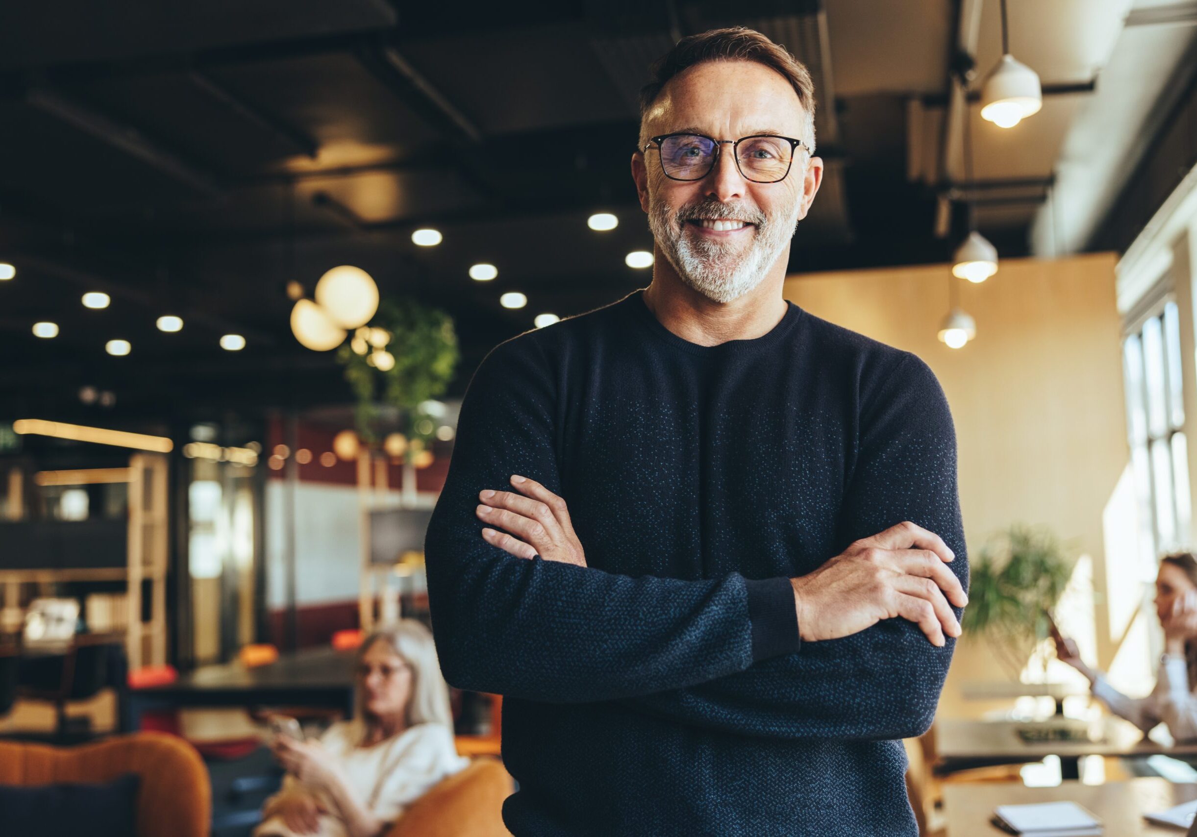 Mature professional standing with arms crossed in a contemporary coworking office environment