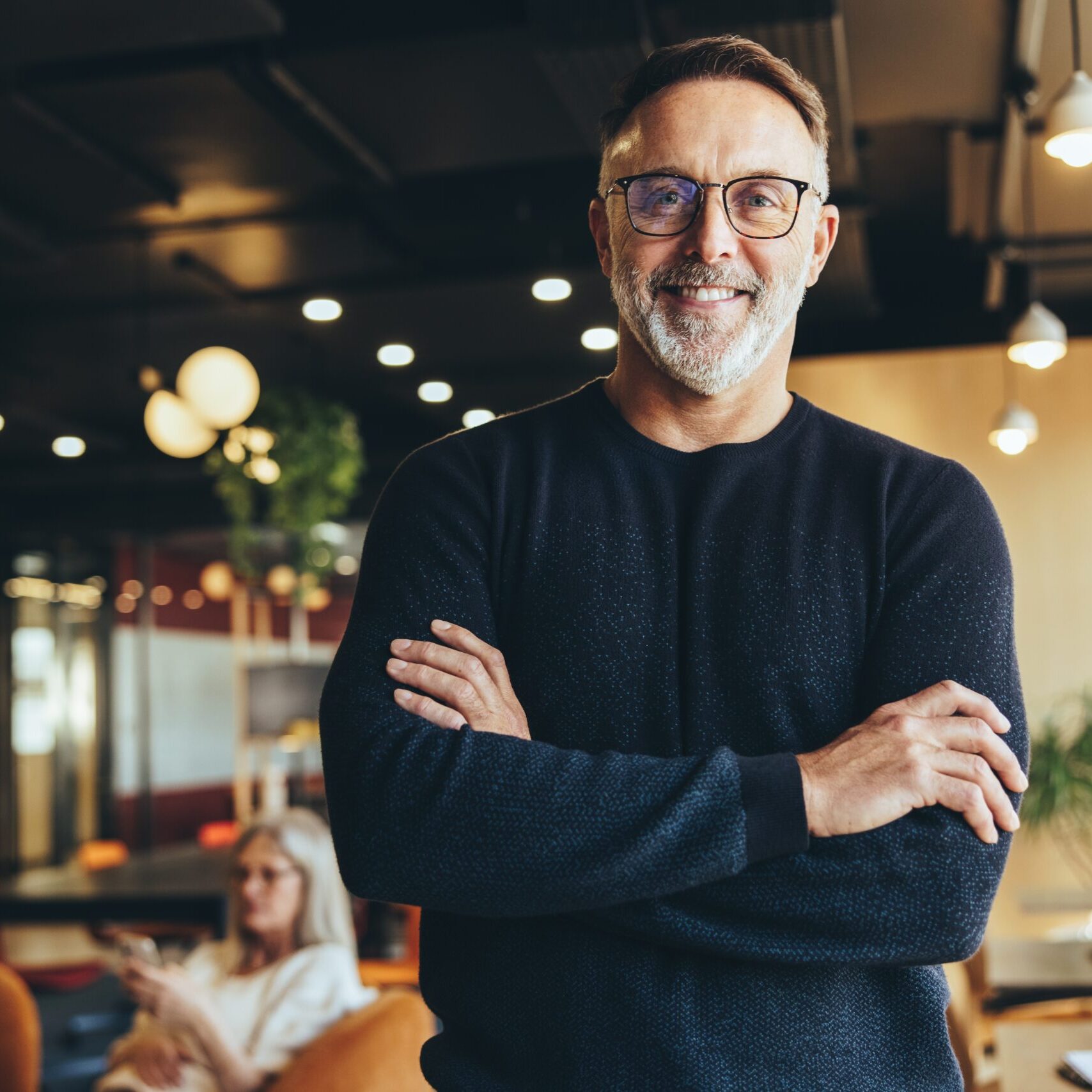 Mature professional standing with arms crossed in a contemporary coworking office environment