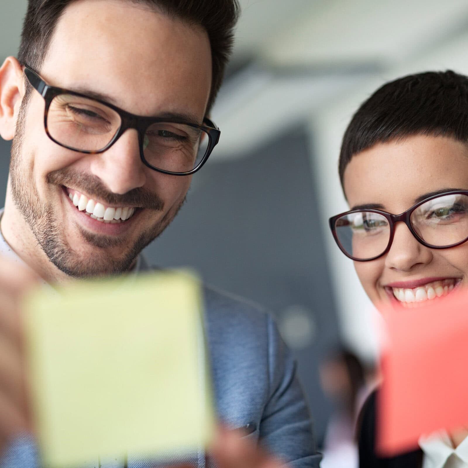 Two smiling business professionals holding sticky notes in an office