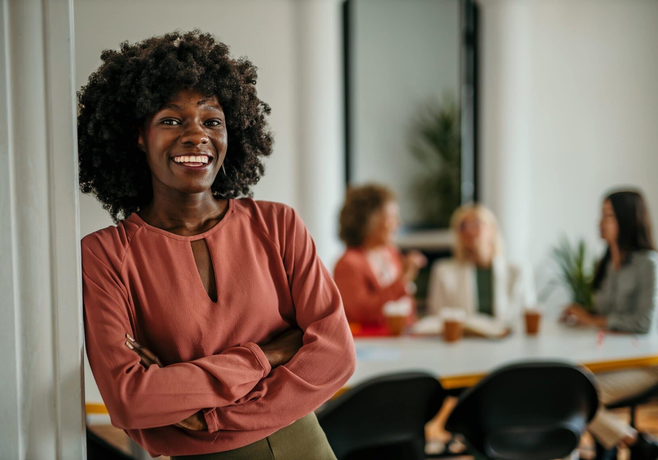 Confident professional standing with arms crossed in front of colleagues meeting in a modern office