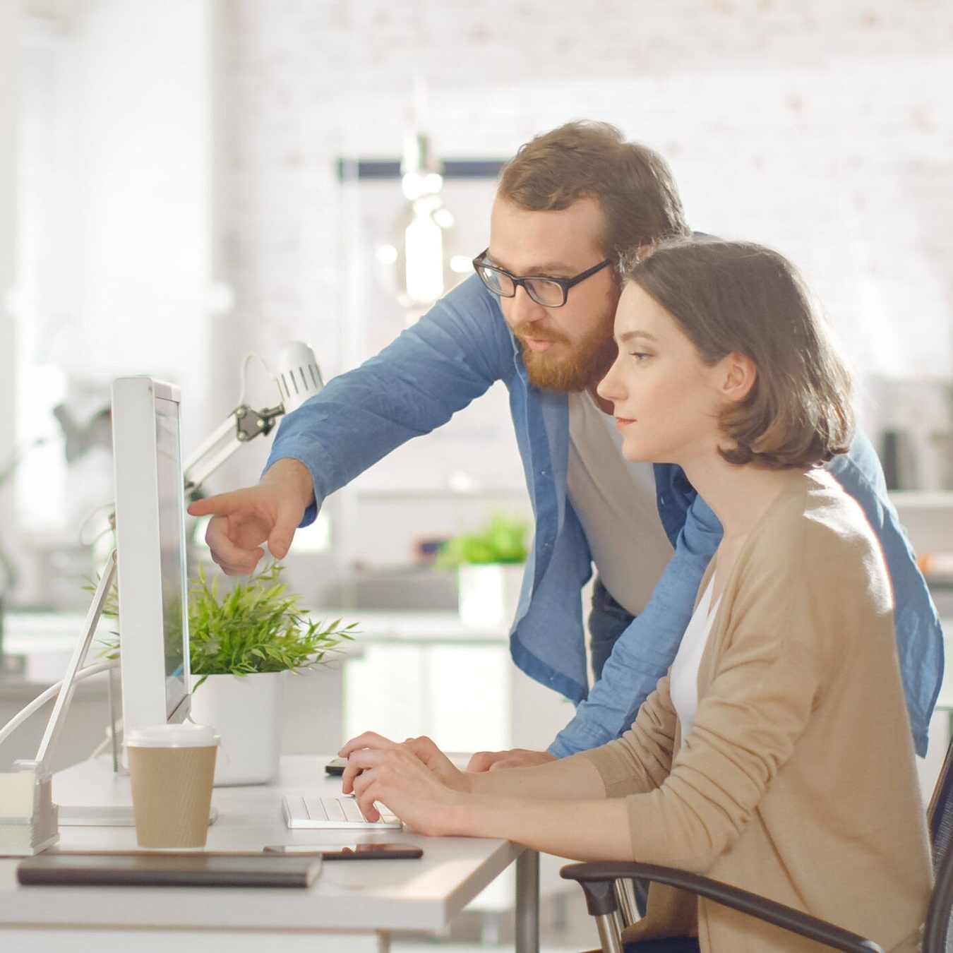 Man pointing at computer screen while colleague works at desk in office