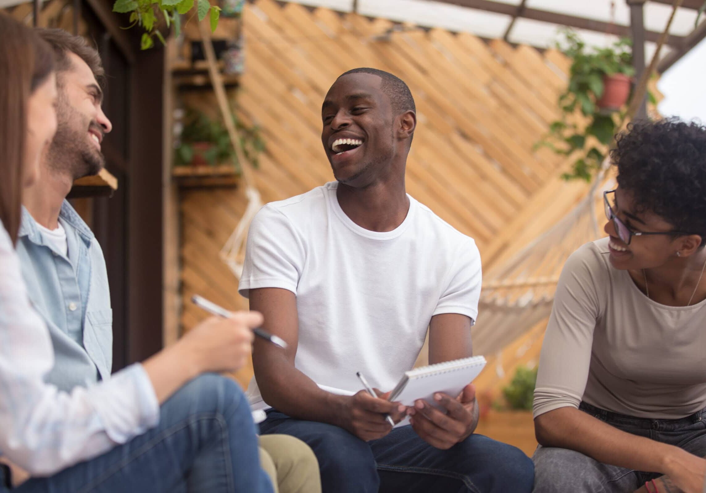 Three colleagues laughing and studying together outdoors with notebooks