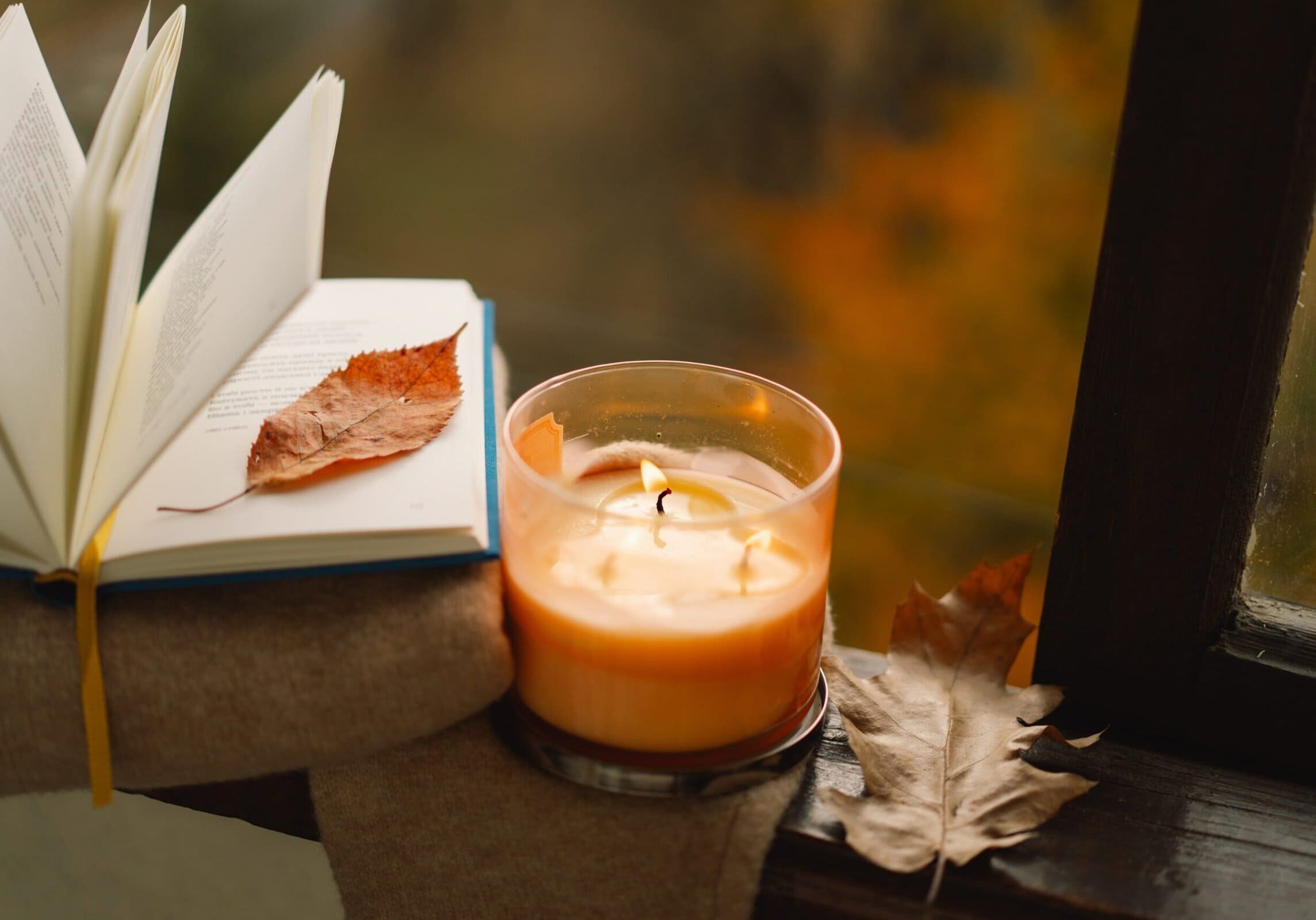 Open book with autumn leaves and lit candle on a windowsill