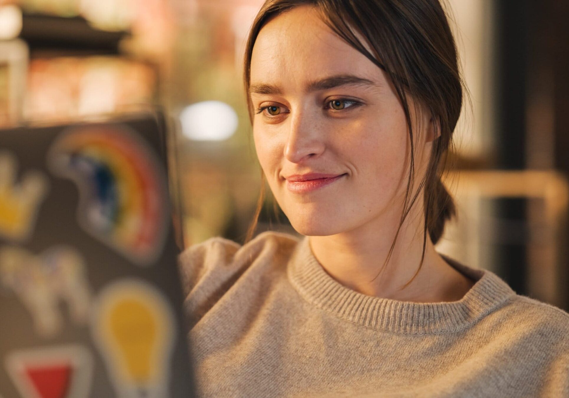 Woman relaxing on a couch while working on a laptop covered in colorful stickers.