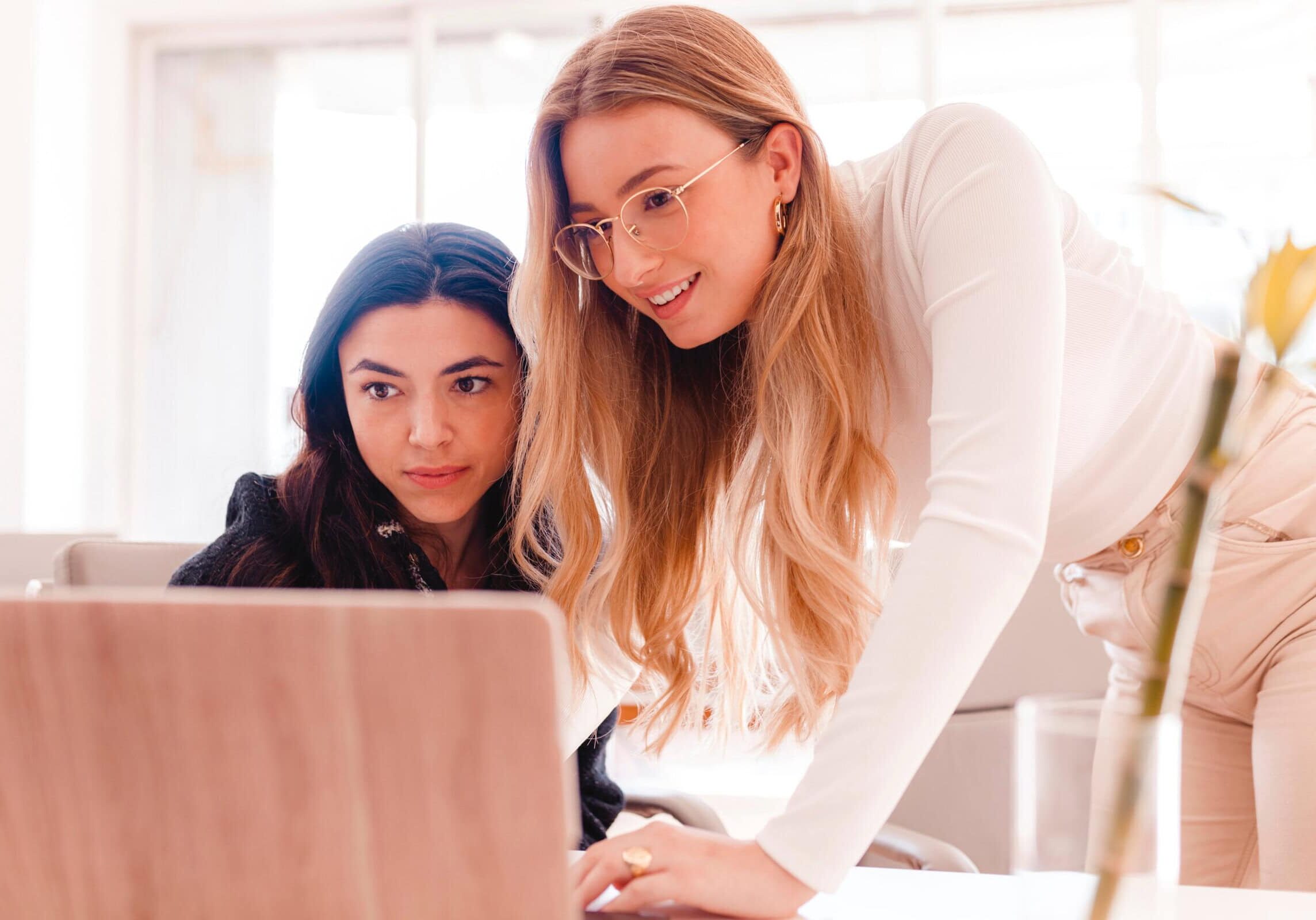 Two women reviewing content together on a laptop in a bright office.