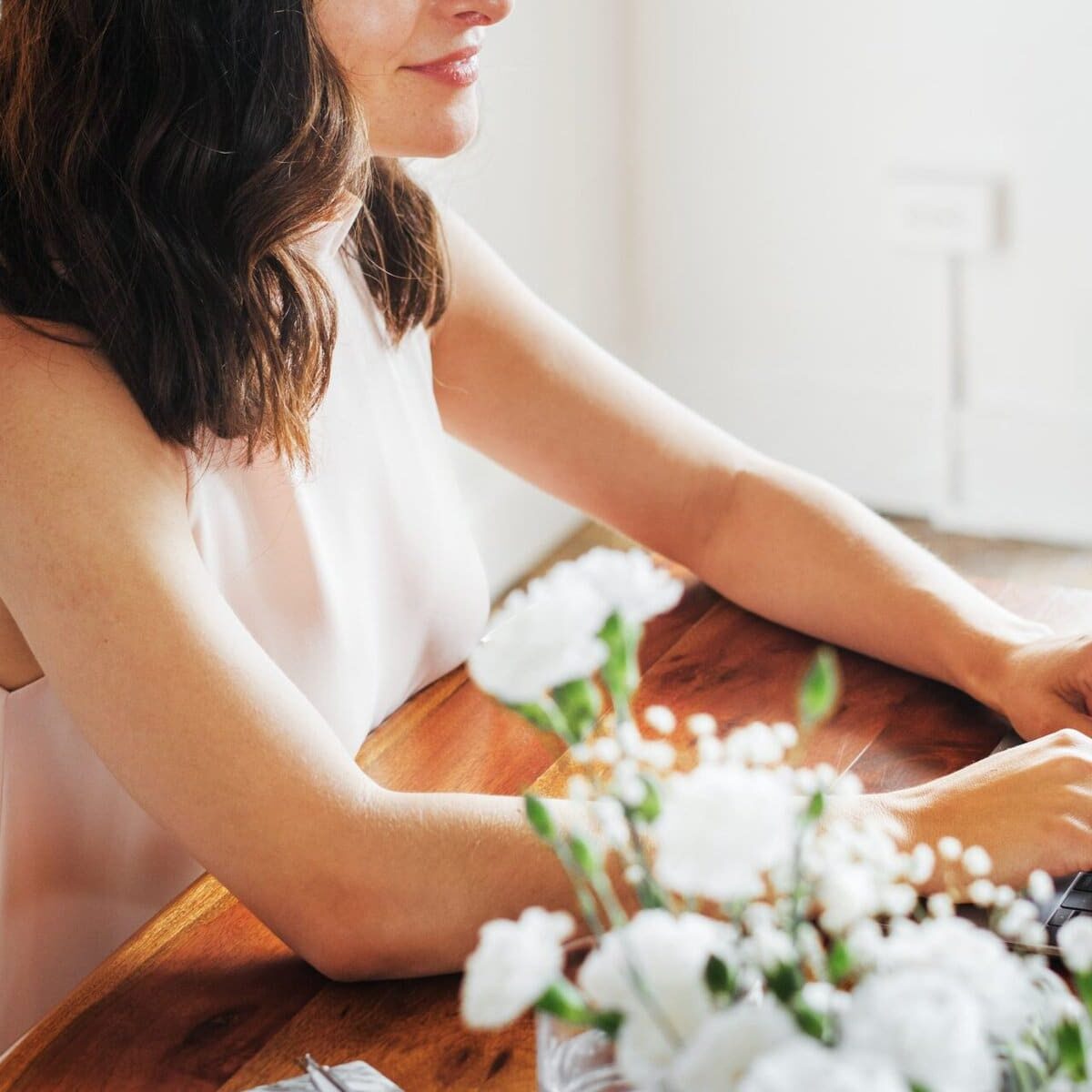 Woman working on laptop at home office desk with flowers nearby