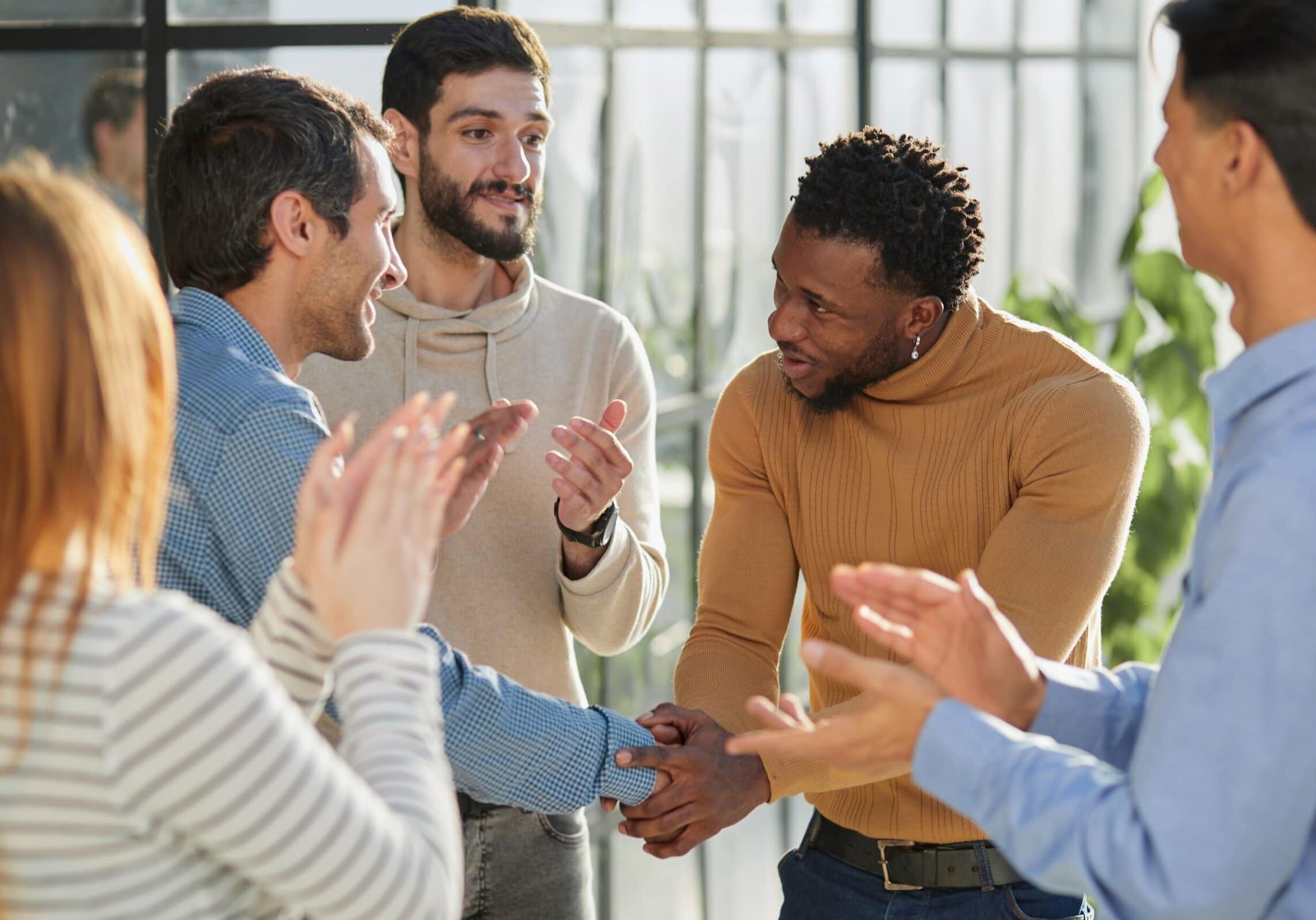 Group of professionals shaking hands and applauding during a workplace networking moment.
