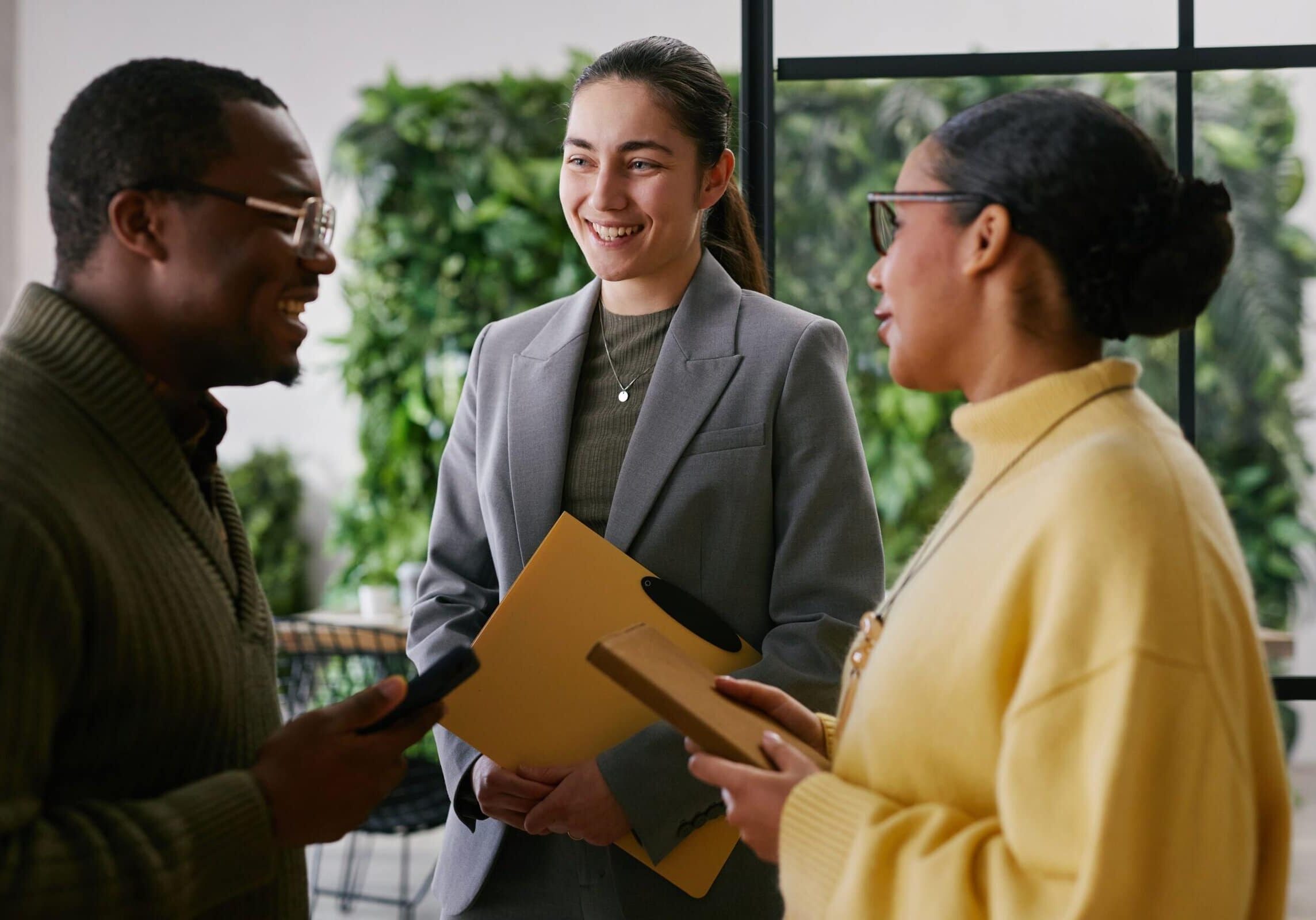 Three professionals talking and smiling during a networking conversation in a modern office.
