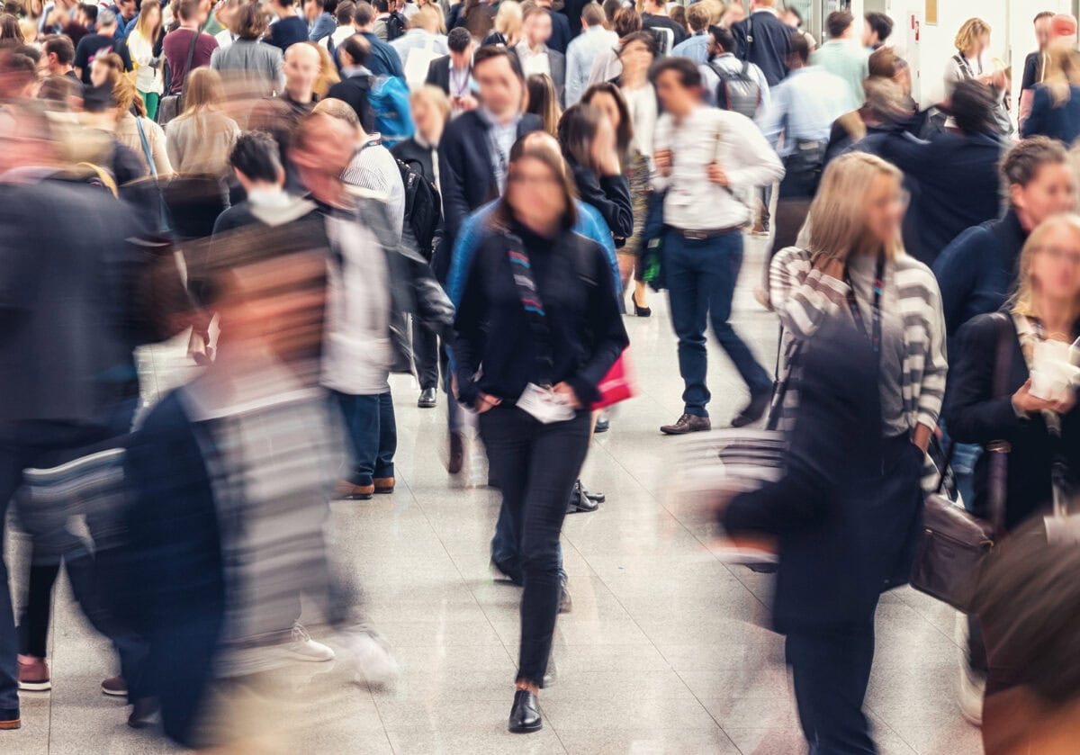 Blurred image of diverse professionals walking through a large conference space, symbolizing connection and global collaboration.