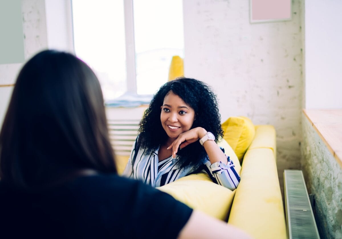  A smiling woman engaged in an attentive, one-on-one coaching conversation on a yellow sofa.