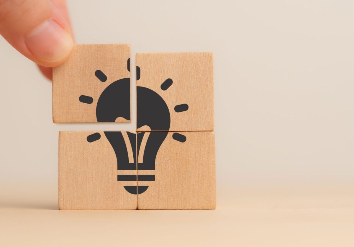 Hand placing a wooden block to complete an image of a light bulb, symbolizing clarity, connection, and integrity in coaching foundations.