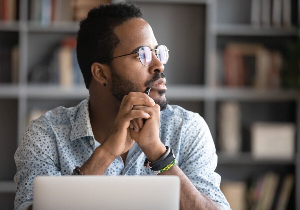 Pensive African American man in glasses distracted from computer work looking into the distance thinking or pondering