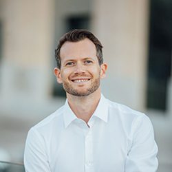 Jan Broders PCC headshot photo, smiling dark haired man wearing a white shirt in front of blurred background