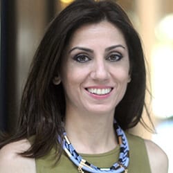 Katrina Kalenidou MCC headshot photo, smiling woman with dark hair wearing blue necklace and green top