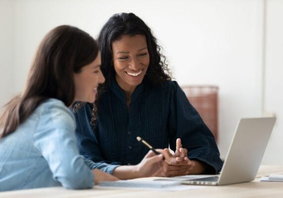 two women looking at a computer smiling on a video call with a coach