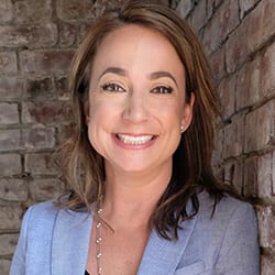 Krista Martin PCC MBA CPCC headshot photo, smiling woman with brown hair wearing a light gray blazer in front of a brick wall