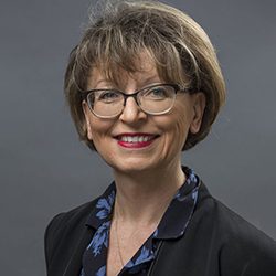 Magdalena Nowicka Mook headshot photo, smiling woman with brown hair wearing glasses and a dark blazer in front of gray background