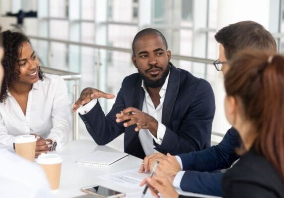 man talking to business peers at a table with all of them listening intently