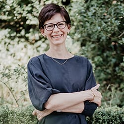 Melissa Birchler headshot photo, smiling short haired woman standing outside with arms crossed over her torso