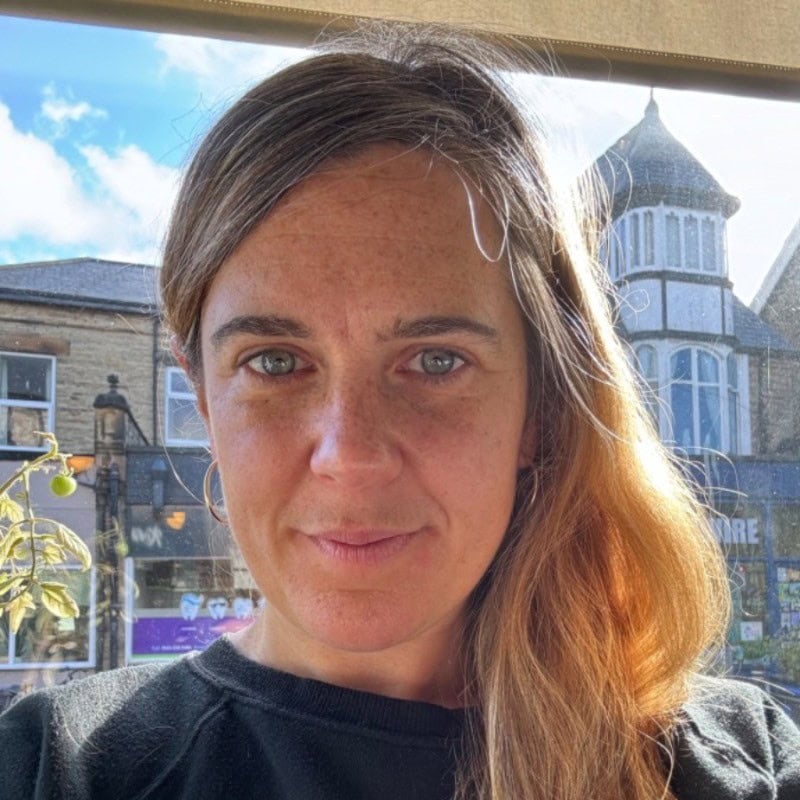 Naomi Whitehead PCC headshot photo, smiling woman with light hair wearing a black top in a town