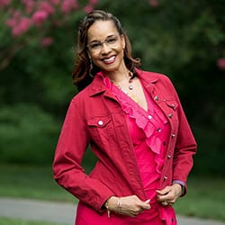 Natalie Jobity headshot photo, smiling dark haired woman in pink standing outside