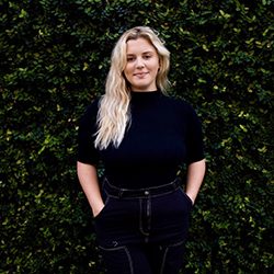 Olivia Melvin headshot photo, blond woman smiling in dark clothing in front of greenery