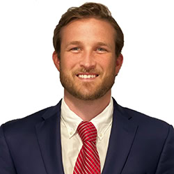Parker Horton headshot photo, brown haired smiling man in navy blazer white shirt and red tie in front of white background