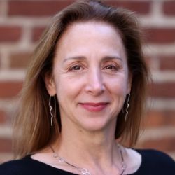 Donna Peters ACC headshot photo, woman with brown hair smiling in front of a blurred brick wall