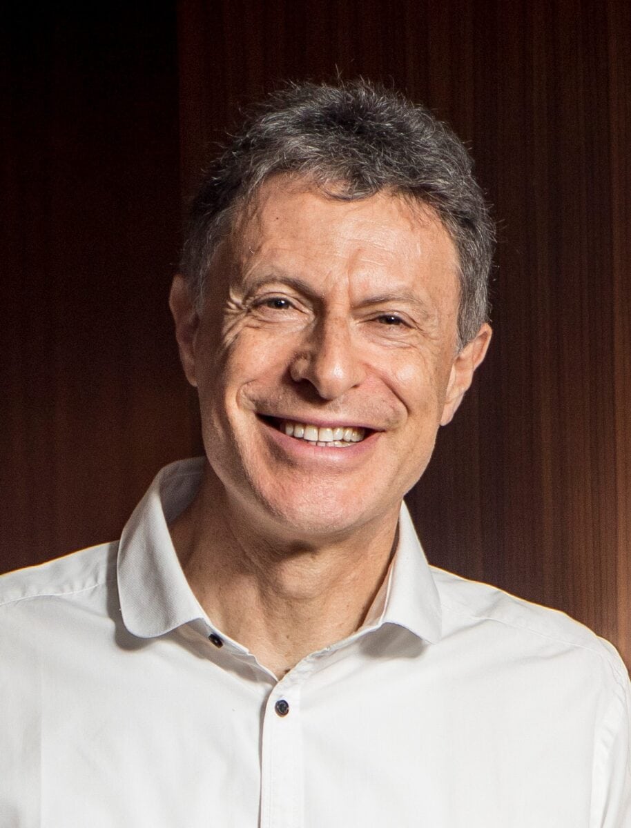 Philippe Rosinski MCC Headshot photo, smiling man wearing white collared shirt in front of brown background