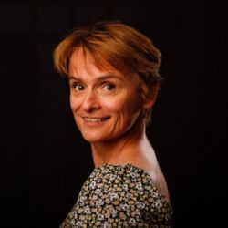 Tanya Podvrsen ACC headshot photo, woman with medium brown short hair and dark flower top smiling dark background