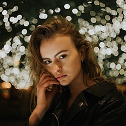 Rebecca Willis headshot photo, woman in dark clothing with her hand on her cheek